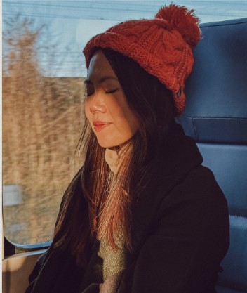 Melissa Toh in a red beanie, sunlit on a train