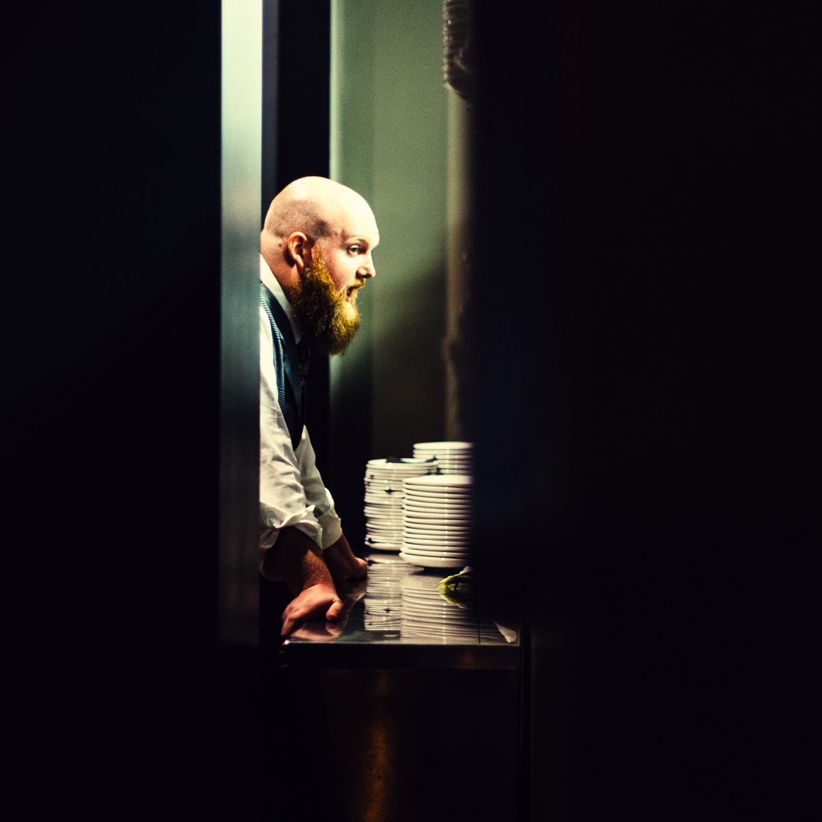 Bald man lit by a sliver of window light