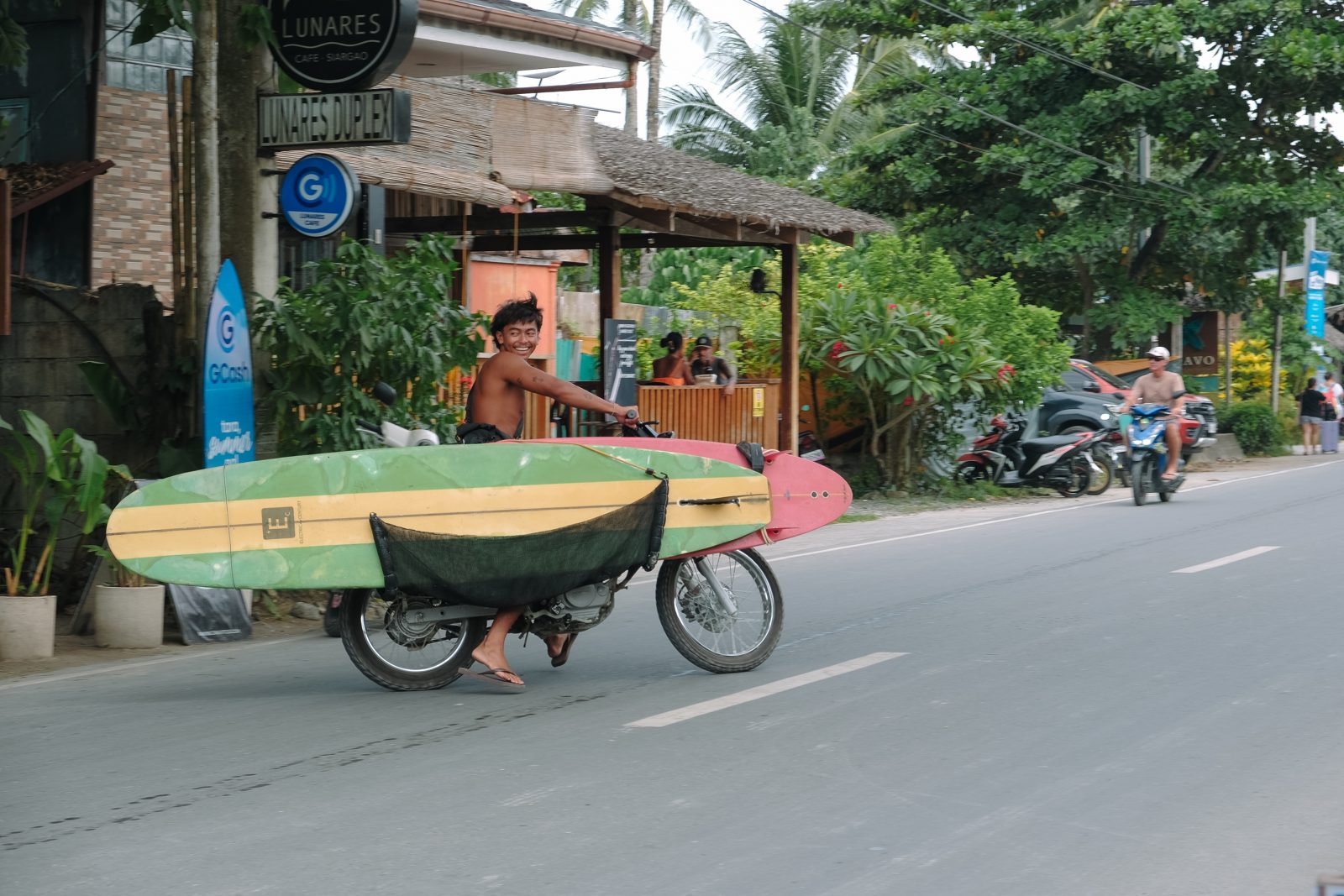 Man wheeling a surfboard trailer down a tropical street