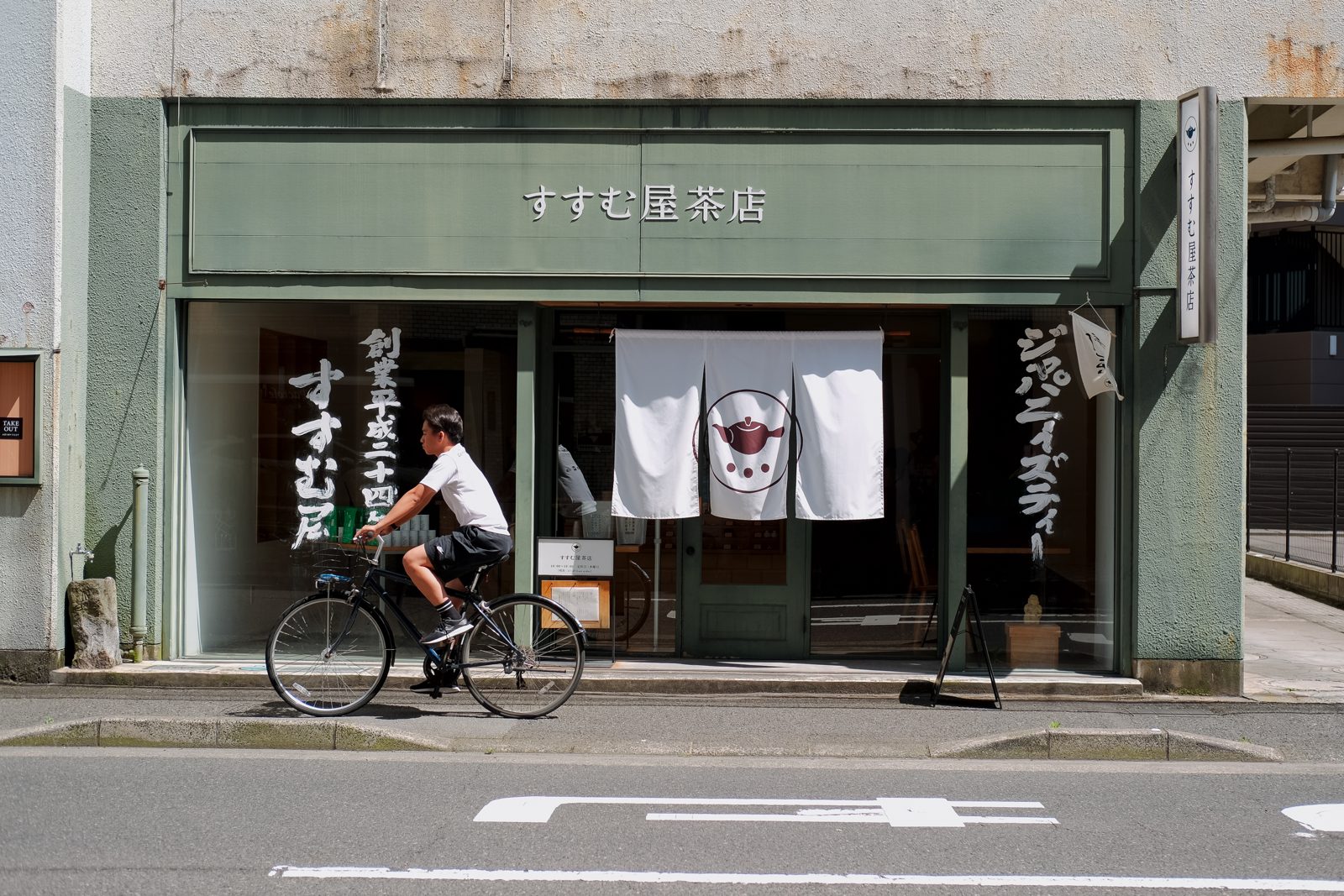Cyclist passing a teahouse storefront